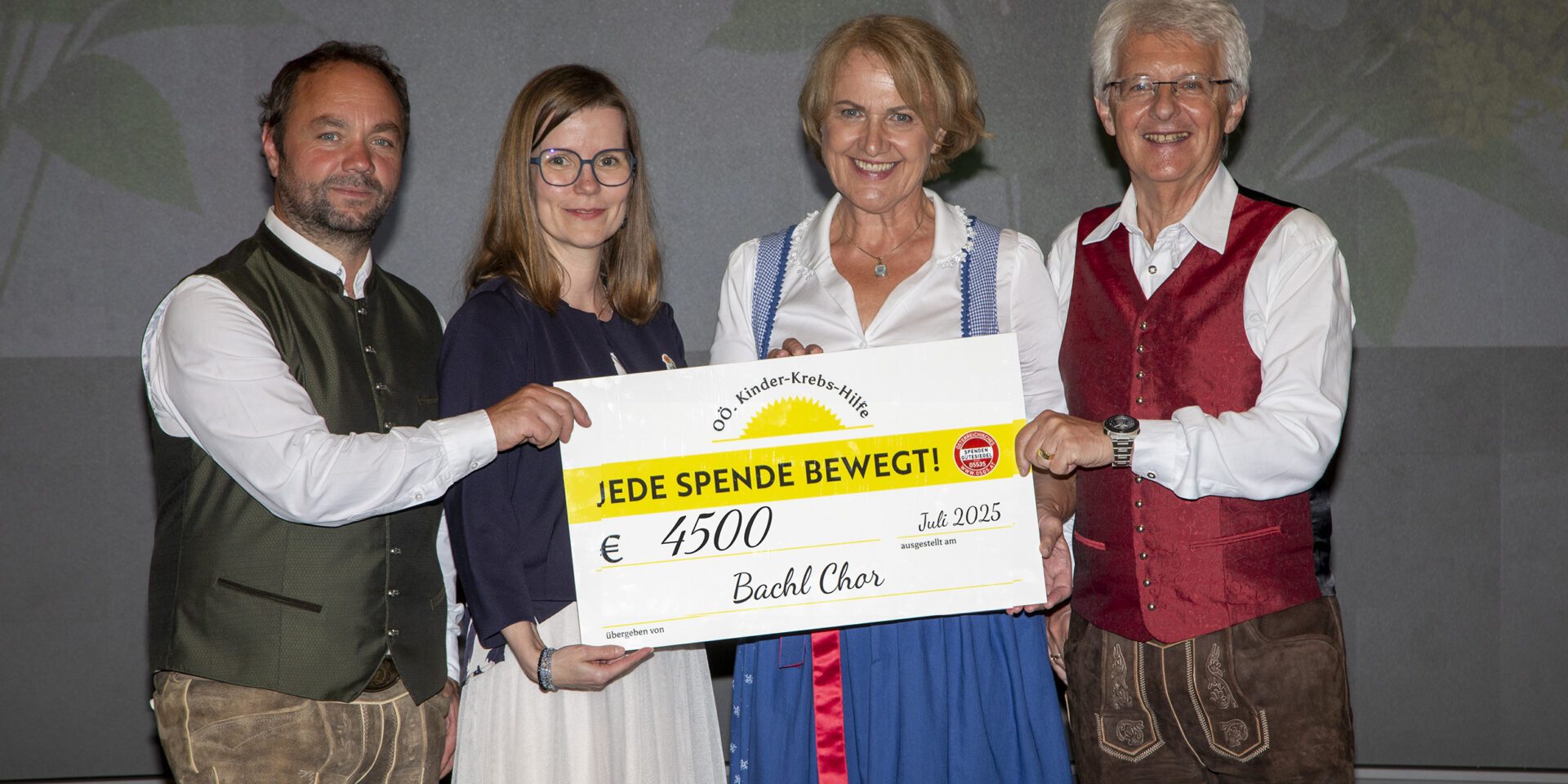 Gruppenfoto mit Scheckübergabe: Von links nach rechts stehen Christian Schmidbauer (Bachl Chor), Katharina Hintersteiner (Vorstandsmitglied der OÖ Kinder-Krebs-Hilfe), Marlene Bremberger und Rudolf Königsecker (beide Bachl Chor). Sie halten gemeinsam einen großen Spendenscheck über €4.500, ausgestellt im Juli 2025 zugunsten der OÖ Kinder-Krebs-Hilfe. Auf dem Scheck steht: „JEDE SPENDE BEWEGT!“. Alle Personen lächeln in die Kamera.