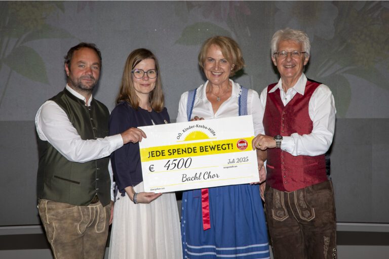 Gruppenfoto mit Scheckübergabe: Von links nach rechts stehen Christian Schmidbauer (Bachl Chor), Katharina Hintersteiner (Vorstandsmitglied der OÖ Kinder-Krebs-Hilfe), Marlene Bremberger und Rudolf Königsecker (beide Bachl Chor). Sie halten gemeinsam einen großen Spendenscheck über €4.500, ausgestellt im Juli 2025 zugunsten der OÖ Kinder-Krebs-Hilfe. Auf dem Scheck steht: „JEDE SPENDE BEWEGT!“. Alle Personen lächeln in die Kamera.