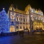 Budapest Parlament beleuchtet, daneben beleuchteter Christbaum