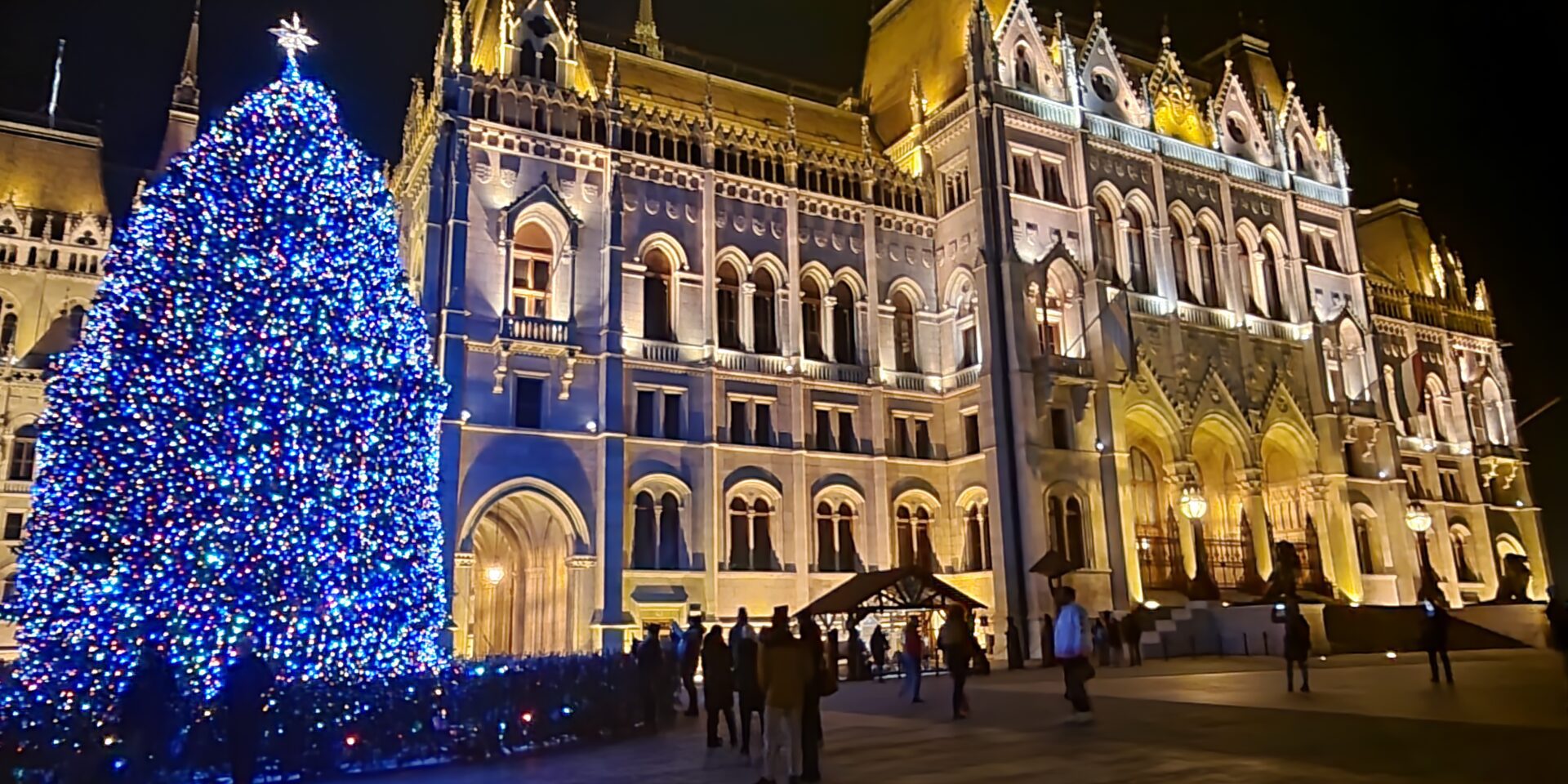 Budapest Parlament beleuchtet, daneben beleuchteter Christbaum