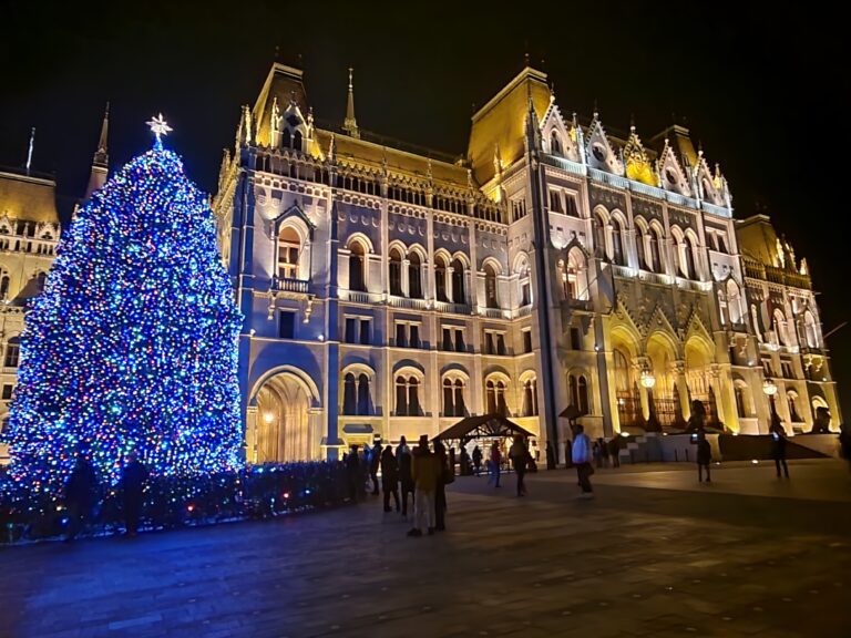 Budapest Parlament beleuchtet, daneben beleuchteter Christbaum